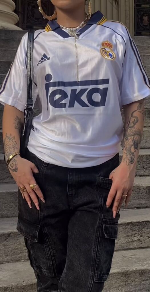 Outfit con una camiseta retro del Real Madrid combinado con unos pantalones cargo negros. Llevar esto es una forma fácil de adoptar el estilo Blokecore en tu día a día.